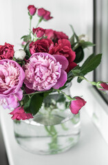 Bouquet with pink and white peonies and garden roses in a vase on a windowsill in a white background.