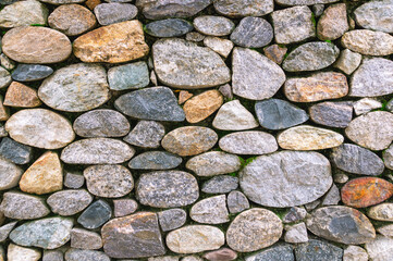 Background of stones. A wall of multicolored stones. The masonry is made of untreated stones. A wall of large stones.
