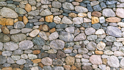 Background of stones. A wall of multicolored stones. The masonry is made of untreated stones. A wall of large stones.