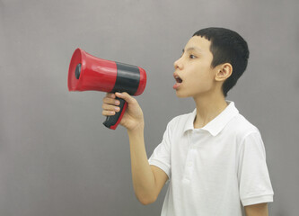 Young asian boy holding megaphone on gray background. Announcement concept. 