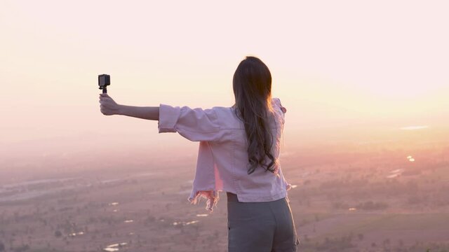 A beautiful blogger or vlogger woman who happily records movie videos and talks about the beautiful nature of the sunset. Social media or content creators share happiness with people.