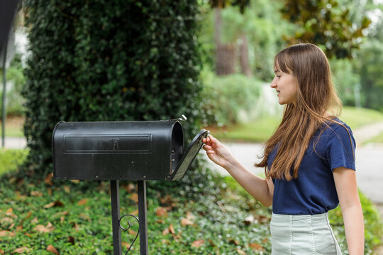 A teen brunette girl with long hair checking the mailbox for letters and packages.