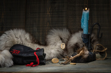 The Algiz rune is a rune of protection. A composition of runes, a dried bird's foot, a burning candle and an old leather bag for Scandinavian runes on the background of an animal skin. selective focus