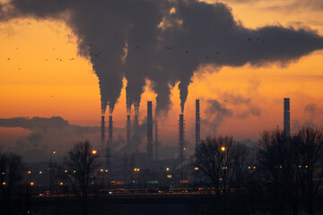 Smoke from heating station in big city during winter season at sunset. Smokestack pipes emitting...