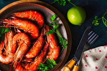 Top view of grilled shrimps and lemon pieces on plate with arranged spices around on black surface