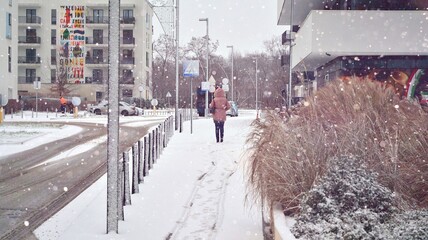 A girl with walks down the street during a heavy snowfall - obrazy, fototapety, plakaty