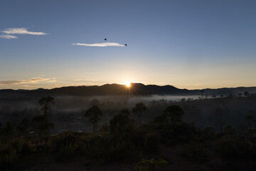 Sunrise behind the mountain with blue sky and a fog in the forest at the foot of the mountain