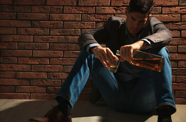 Addicted man with alcoholic drink near red brick wall. Space for text