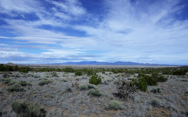  Expansive New Mexico landscape with scrubland in the foreground and mountains and town with lots of blue sky and clouds in the background