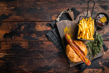 Currywurst Bratwurst sausage in a bun with curry sauce and French fries. Wooden background. Top...
