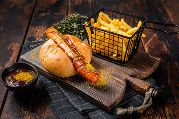 Fototapeta Currywurst Bratwurst sausage in a bun with curry sauce and French fries. Wooden background. Top view obraz