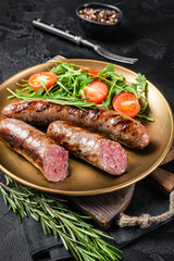 Roasted meat sausages with arugula and tomato salad. Black background. Top view