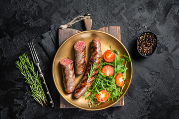 Roasted meat sausages with arugula and tomato salad. Black background. Top view