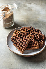 Chocolate waffles in the shape of a heart in ceramic plate on textured background with a can of cocoa in the background, still life for valentine's day