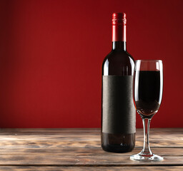 Red wine with a transparent high glass on a light wooden table. A bottle of wine in the background. Red background. Place for text