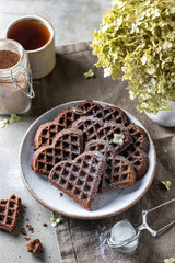 Chocolate waffles in the shape of a heart in ceramic plate on textured background, still life for valentine's day