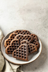 Chocolate waffles in the shape of a heart in ceramic plate on textured background with a linen...