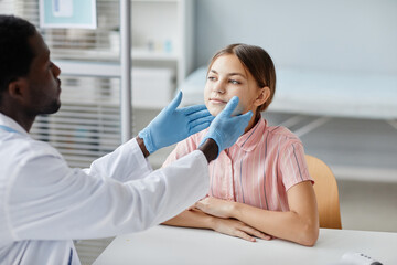 Portrait of African-American doctor examining little girl during consultation at pediatric clinic