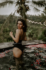 Fototapeta premium Young traveller relaxing by the pool in a hotel in Bali, surrounded by jungle, palm trees and green landscapes.