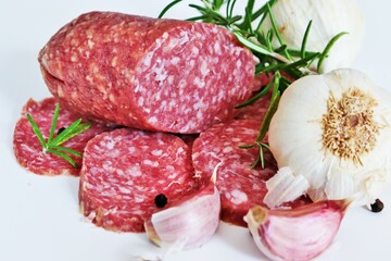 Traditional smoked salami sausages sliced with pepper, garlic and rosemary on wooden cutting board.