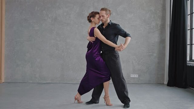 Man and woman are sensually doing tango pose in grey studio, looking eye to eye. Full growth shot of people dancing. Slow motion dancing tango. High quality 4k footage