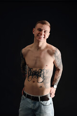 Smiling shirtless young man with tattoos on black background