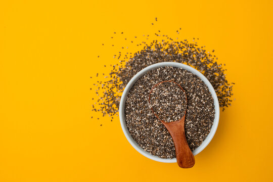 Glass bowl and wood spoon with chia seed son a bright yellow background, closeup, view from above