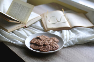 Plate of healthy gluten free cookies, open books and reading glasses on the table. Selective focus.