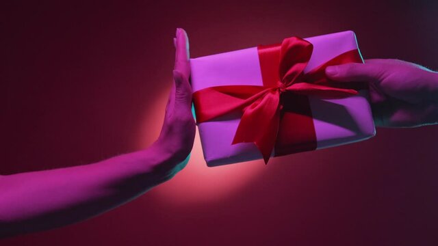 Gift refuse. Couple disagreement. Holidays fail. Female hand protesting to get present with ruby ribbon from male on red purple neon light halo spotlight background.
