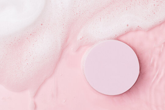 Top view of pink transparent clear calm water surface. Texture with splashes, foam and bubbles with pink podium. Trendy abstract spring summer nature background for product. Flat lay cosmetic mockup