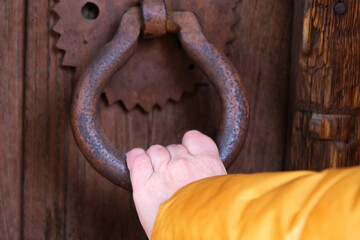 Female hand knocking on the door with ancient iron doorknob, woman opening the wooden door with bronze rusty handle.