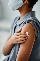 Vertical close up of African-American child getting vaccinated in clinic and holding sterile cotton ball on shoulder