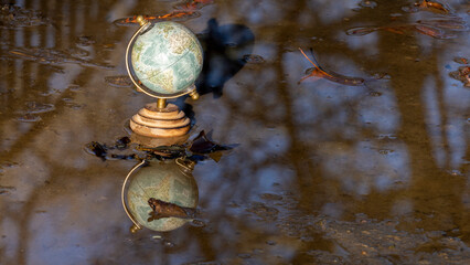Pretty terrestrial globe in wood and metal, placed in a puddle outside, and its reflection, and...