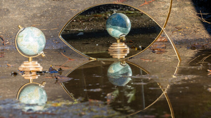 Terrestrial globe placed in a puddle on the ground, mirror in the background, multiple reflections