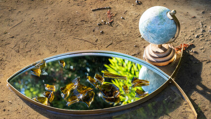 Mirror on the floor covered with dark glass fragments and glimpse of part of the terrestrial globe
