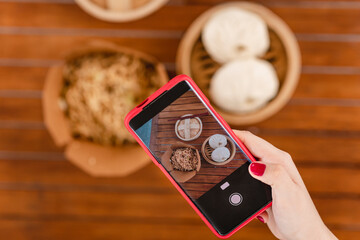 Mano de una mujer caucásica con un teléfono celular tomando una foto de la comida china en su mesa.	
 - obrazy, fototapety, plakaty
