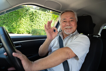 Asian senior man sitting in car and showing ok sign