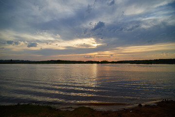 Evening sky with dramatic clouds and sunset over the river or lake. Dramatic sunset over dark water