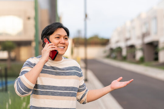 Hombre asiático conversando por celular en exterior con las manos extendidas
