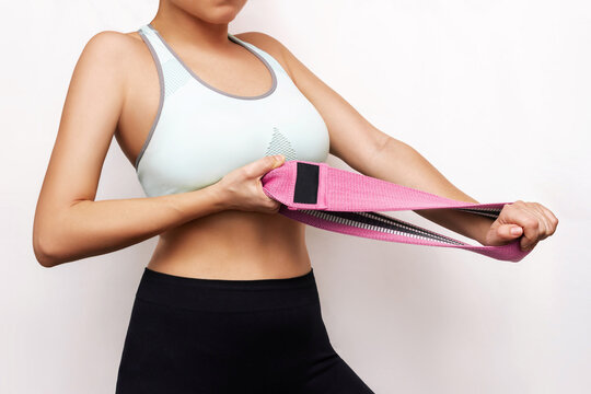 Cropped shot of young toned slim woman doing hand exercises with a pink fitness elastic resistance band isolated on white background. Workout for the upper body, arms, back, chest. Healthy lifestyle
