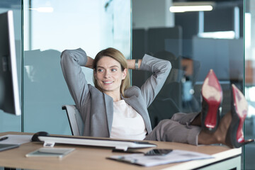 Woman director resting and dreaming at work, business woman throwing her hands behind her head and feet on the table, resting on the day at work