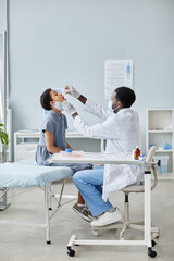 Vertical side view of African-American of doctor dropping liquid in mouth of child during oral...