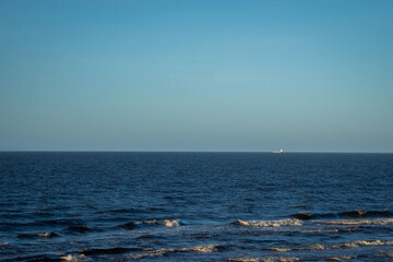 Sea landscape with blue water and waves with white foam. A transport ship can be seen in the distance on the horizon.
