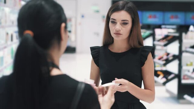 Front view of young woman talking with shop assistant in cosmetics store. Caucasian brunette needs help with choosing and seller is glad to give an advice. High quality 4k footage