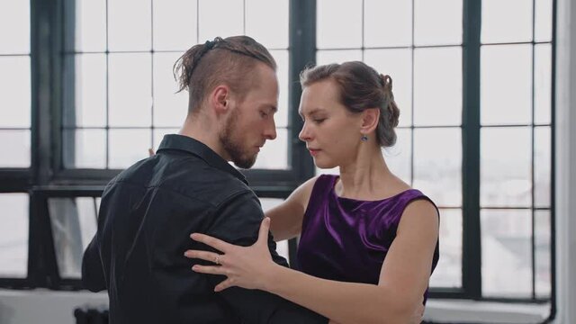 Close shot of couple dancing tango in grey studio against large windows. People face to face dancing romantic dance. Slow motion dancing tango. High quality 4k footage