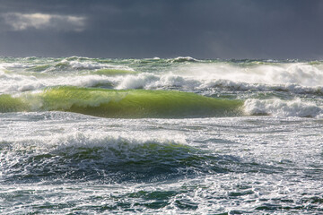 The green waves of the stormy Baltic Sea with lots of spray beneath dark gray rain clouds