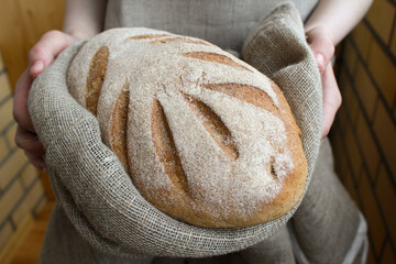 Female hands holding loaf of homemade rye bread on towel. Woman holds beautifully decorated bread