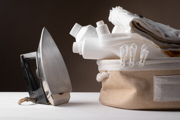 Old retro style electric iron, detergent bottles and towel on the table, front view. Laundry.