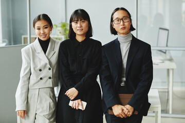 Waist up portrait of three Asian business people looking at camera while standing in office