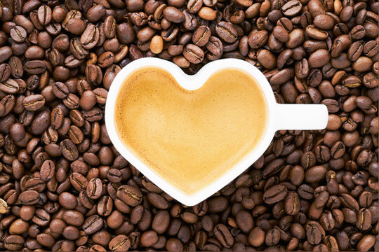 Coffee in heart shape mug on coffee beans background. Valentine's day concept. Top view, copy space